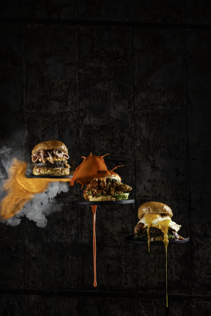 Three mouthwatering burgers with unique toppings float against a dark, smoky backdrop in Atlanta, Georgia.