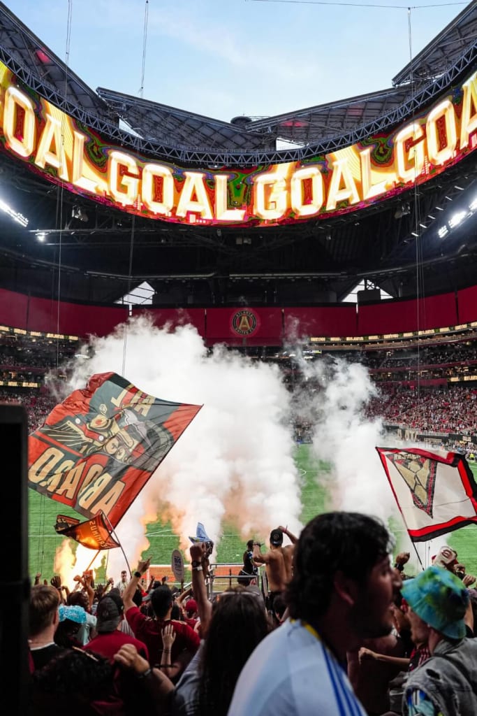 A crowded stadium with fans waving flags and smoke filling the air in Atlanta, Georgia.