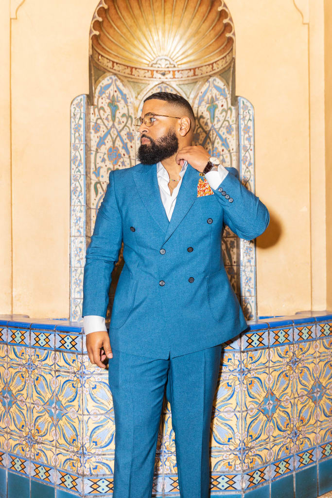 A man in a blue suit stands confidently against a backdrop of ornate, colorful tiles in Atlanta, Georgia.
