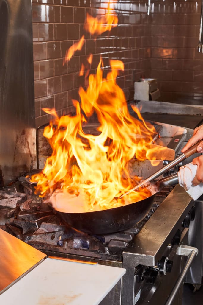A chef stirs a wok over an open flame in a professional kitchen in Atlanta, Georgia.