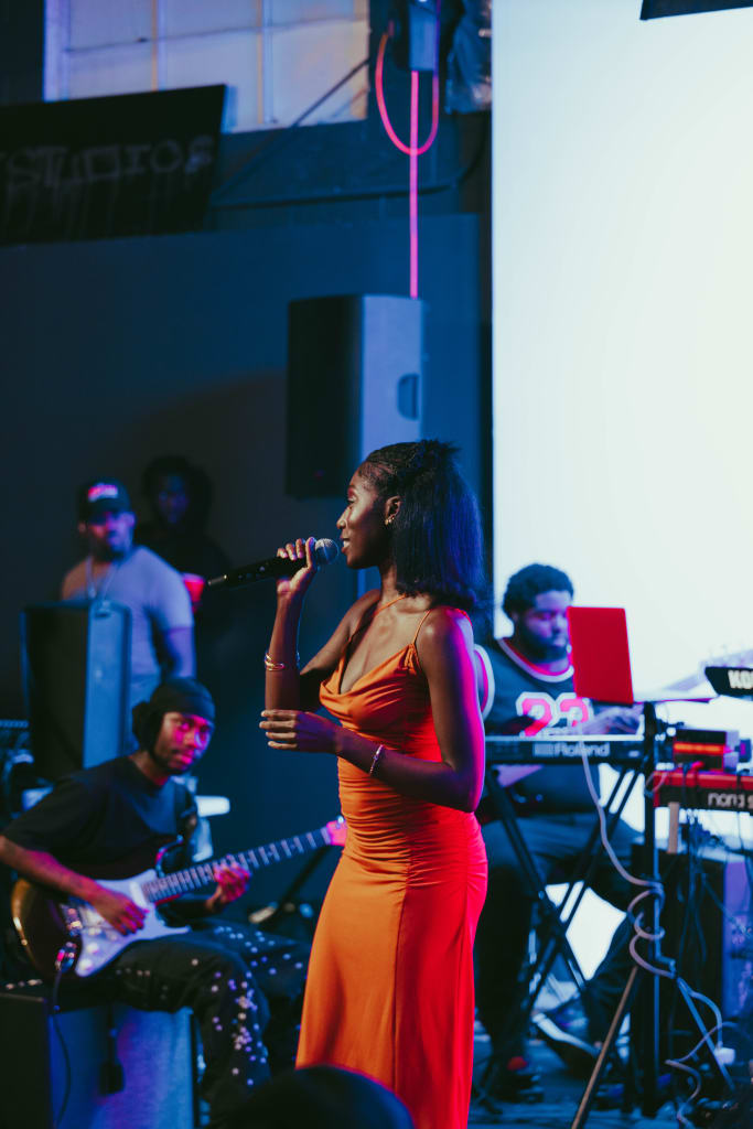 A woman in a red dress sings into a microphone on stage with a band behind her in Atlanta, Georgia.