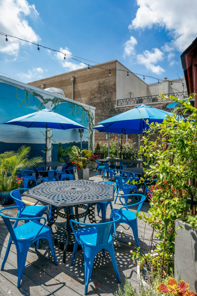 A vibrant outdoor patio features blue metal furniture, lush greenery, and colorful flowers under a clear blue sky in Atlanta, Georgia.