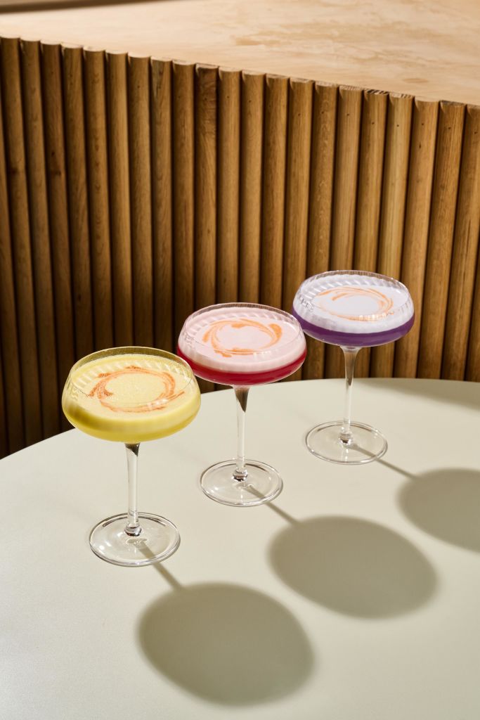 Must-Try Summer Cocktails in Atlanta 6 Three colorful cocktails with swirled foam tops sit on a table against a wooden backdrop in Atlanta, Georgia.