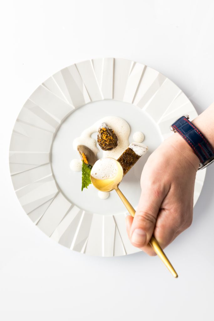Where to Dine with a Large Group at Atlanta’s Michelin Guide Restaurants 1 A hand with a gold spoon hovers over a white plate with a geometric design, holding a small, artfully arranged dish in Atlanta, Georgia.