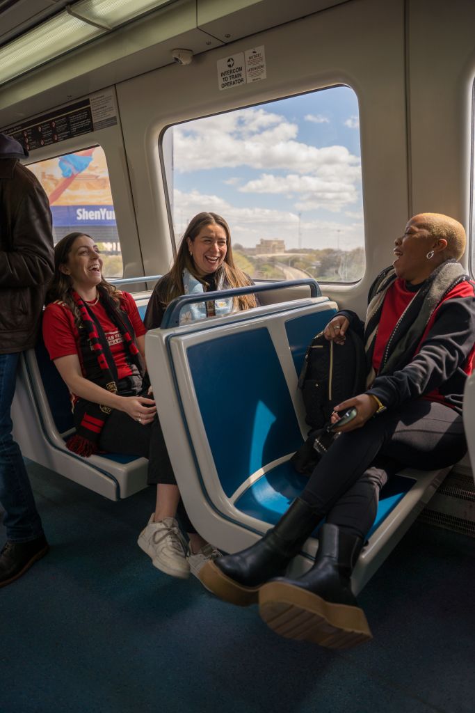 Guide to Exploring Atlanta on MARTA Trains (From a Local) 4 Three women laugh and chat on a train with blue seats and a view of the sky in Atlanta, Georgia.