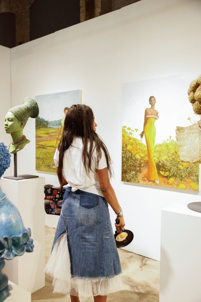 Ultimate Guide to Atlanta Art Fair 2026 3 A woman in a denim skirt and white top stands in an art gallery, admiring paintings and sculptures in Atlanta, Georgia.