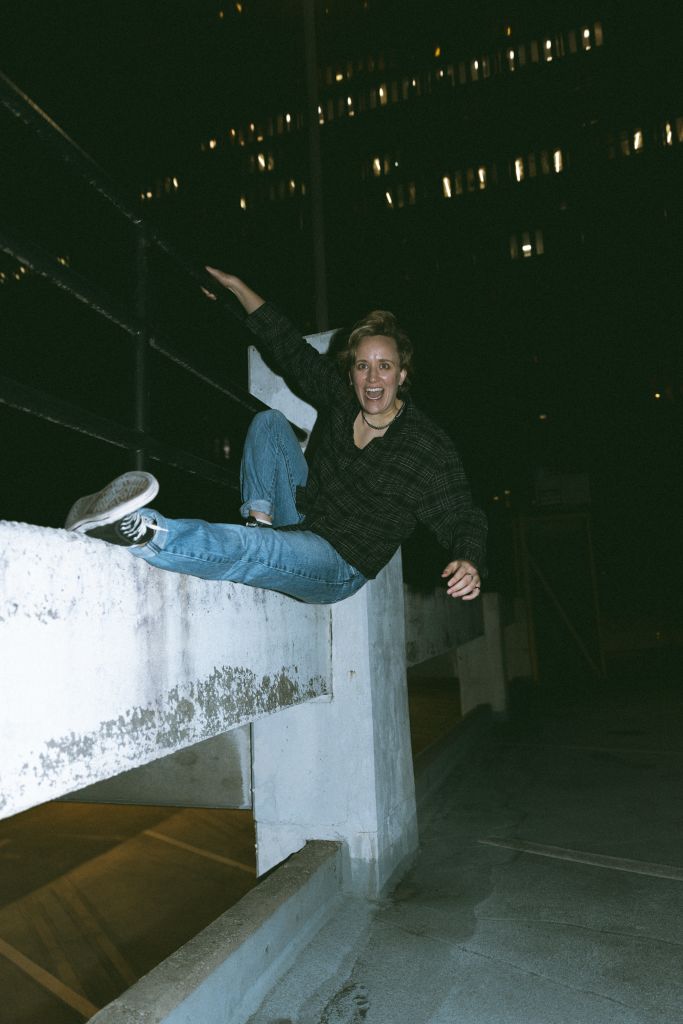 A person is perched on a concrete ledge, arms outstretched, with a cityscape of illuminated buildings in the background in Atlanta, Georgia.