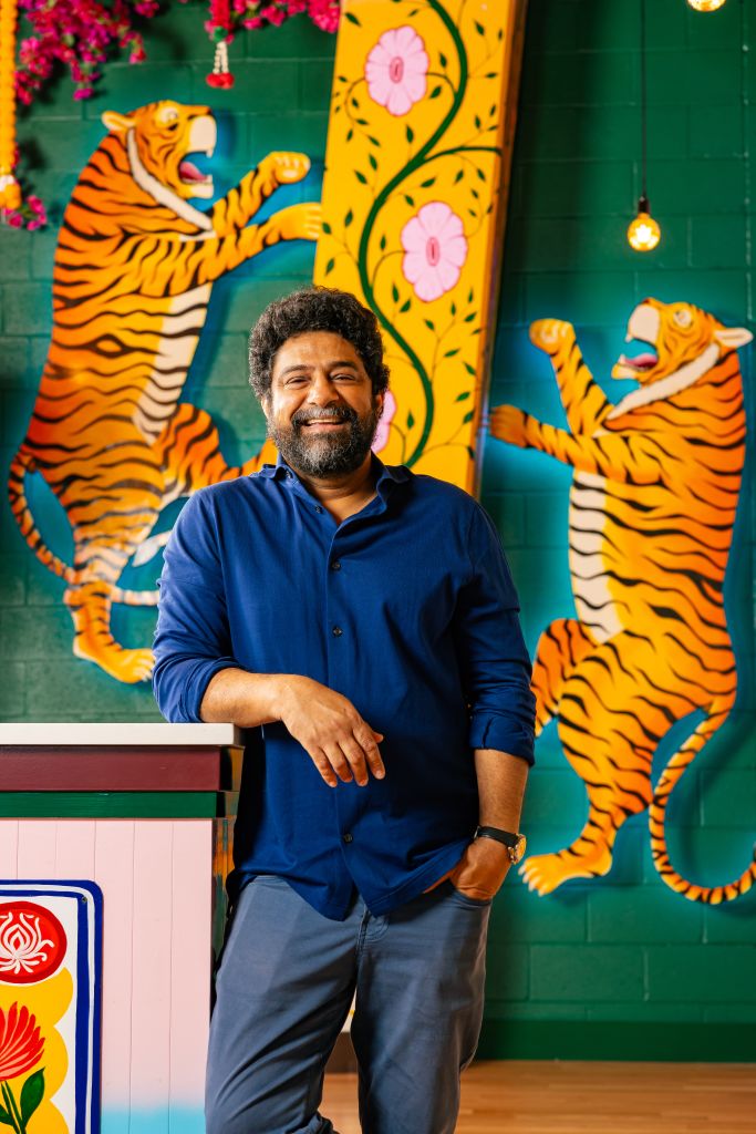 A man stands confidently in front of a vibrant mural featuring two playful tigers and intricate floral designs in Atlanta, Georgia.