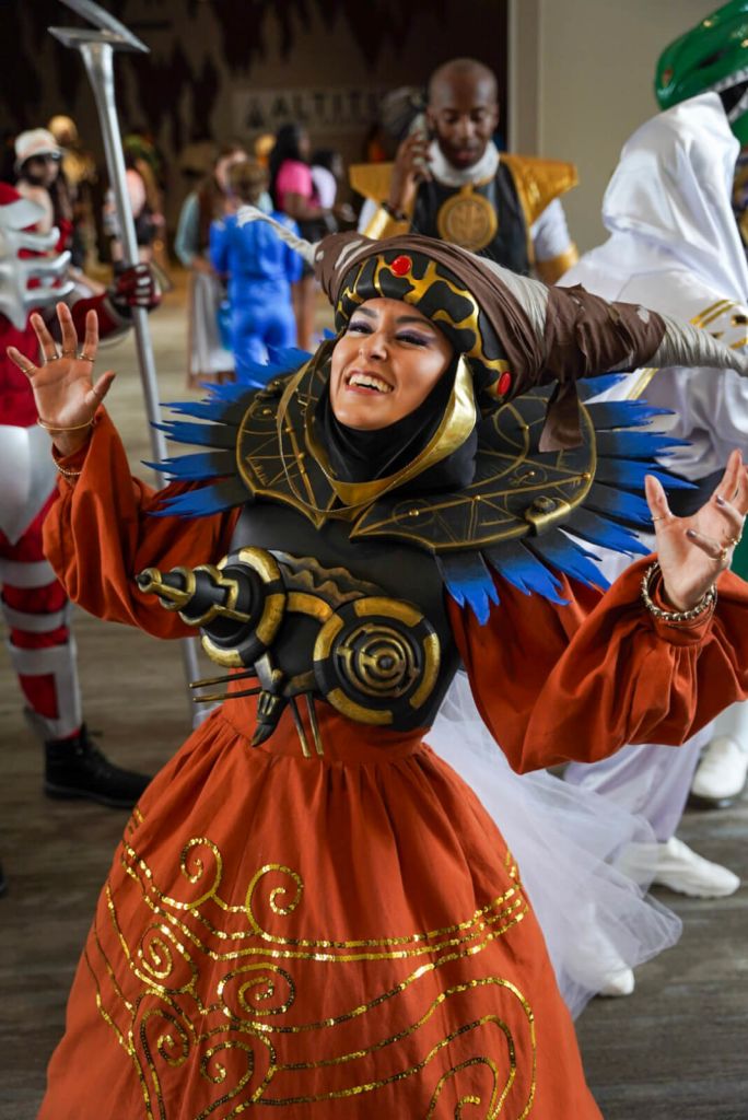 Fun Facts About Dragon Con that you Probably Didn’t Know 3 A person in a vibrant orange dress with gold swirls and a large, ornate headdress dances joyfully in Atlanta, Georgia.