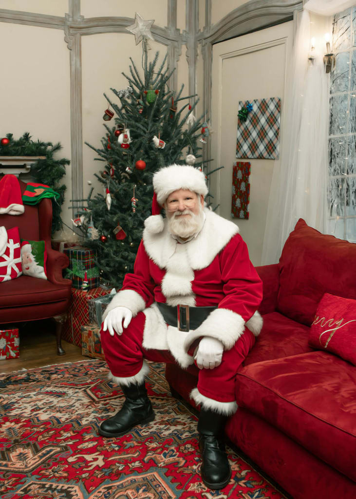 Cool Things To Do in December in Atlanta 5 Santa Claus sits on a red couch in a festive living room with a Christmas tree in Atlanta, Georgia.