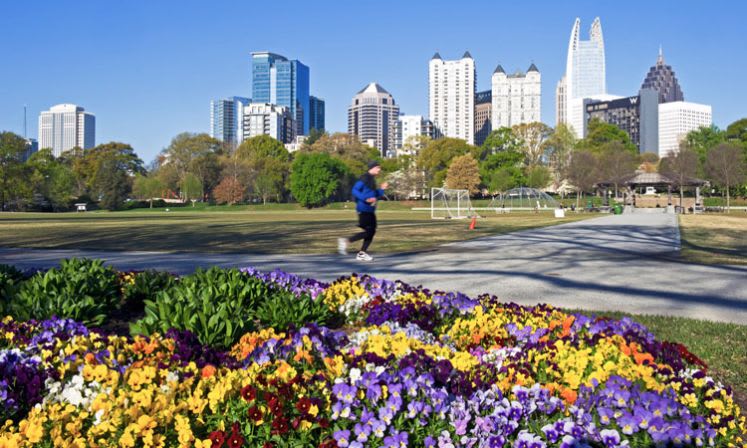 Parks & Venues 2 A runner jogs through a park with colorful flower beds and a city skyline in the background in Atlanta, Georgia.
