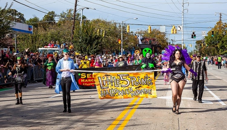 A vibrant Halloween parade featuring costumed participants carrying a 'Little 5 Points Halloween Parade' banner in Atlanta, Georgia.