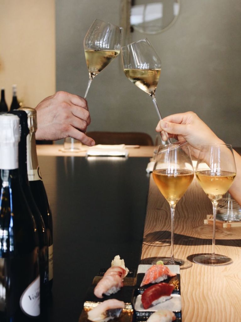 Two people clink champagne glasses at a sushi restaurant, celebrating with wine and sashimi in Atlanta, Georgia.