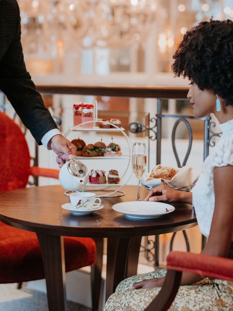 A woman in a floral dress enjoys afternoon tea with a man in a suit at a round table in Atlanta, Georgia.