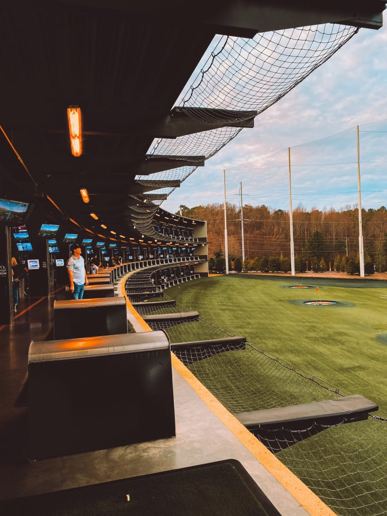 A modern indoor golf driving range with a curved ceiling and artificial turf in Atlanta, Georgia.