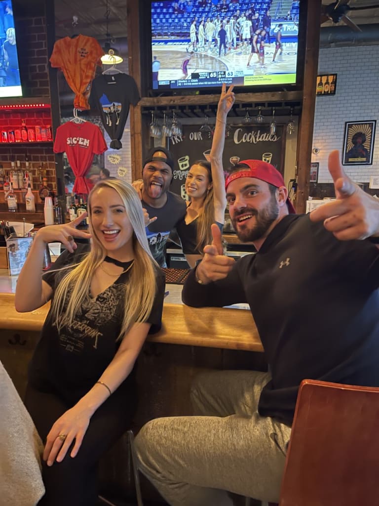 A group of five friends, three men and two women, are posing for a photo at a bar in Atlanta, Georgia.