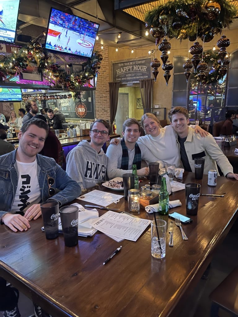 Five young men gather around a wooden table at a lively sports bar, enjoying drinks and conversation in Atlanta, Georgia.
