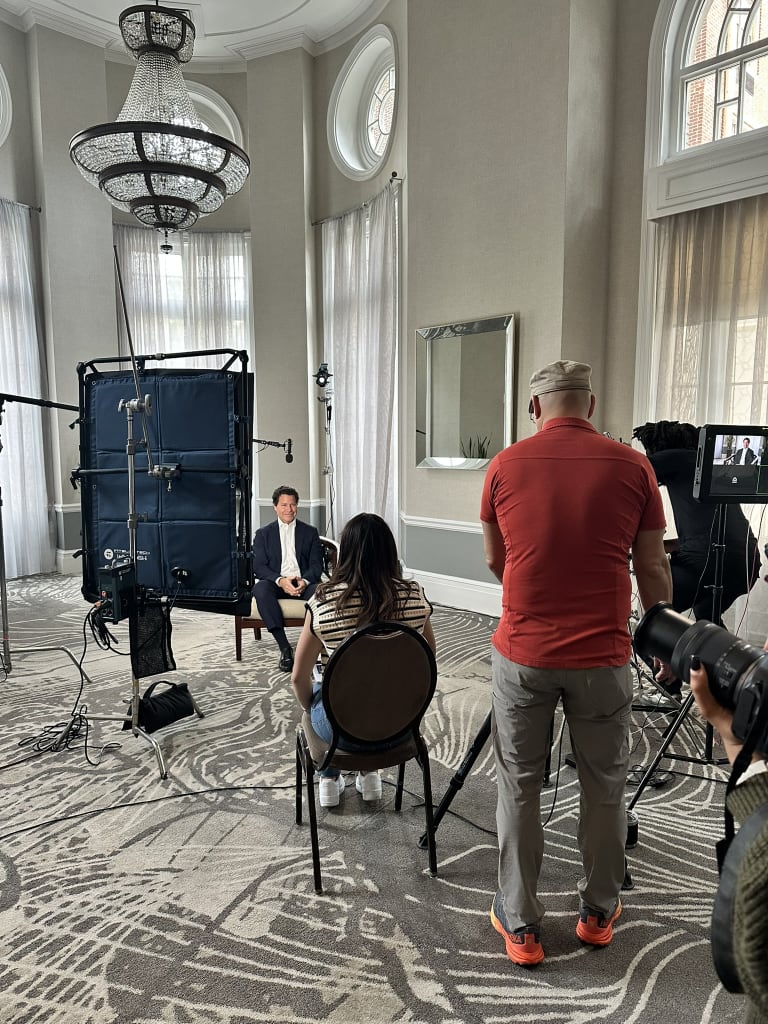 A film crew is setting up equipment in a grand room with a chandelier and large windows in Atlanta, Georgia.