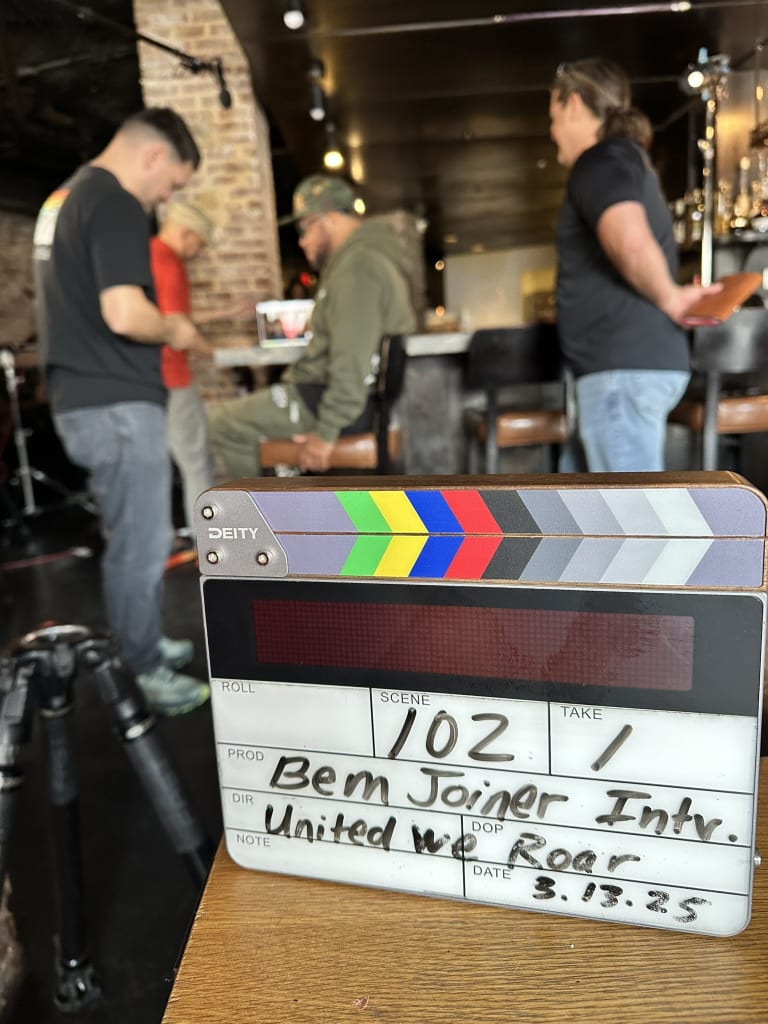 United We Roar 9 A clapperboard with the scene number 102 and the word 'Take' is placed on a wooden table in Atlanta, Georgia.