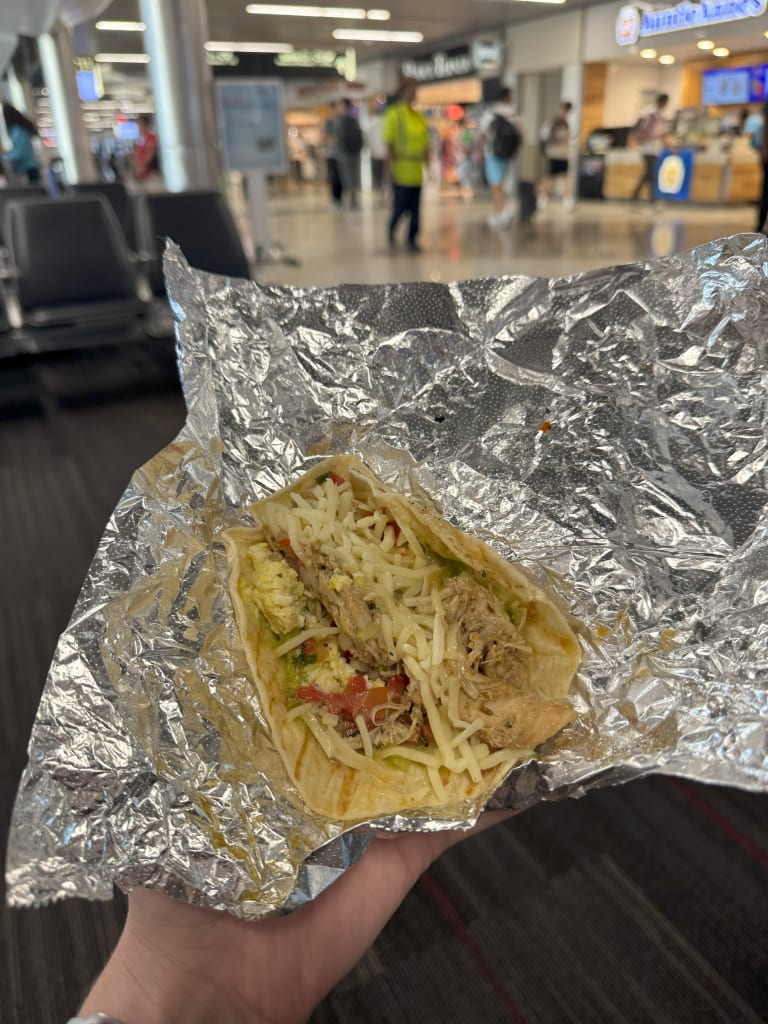 Where to Dine at Hartsfield-Jackson Atlanta International Airport 4 A hand holds a taco wrapped in aluminum foil, with visible ingredients including shredded meat and cheese in Atlanta, Georgia.