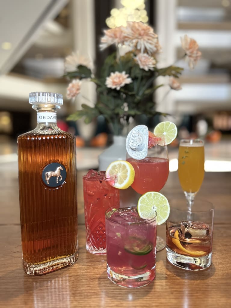Ultimate Guide to Attending Beyoncé's Cowboy Carter Tour in Atlanta 2 Assorted colorful cocktails and a bottle of SirDavids whiskey on a wooden table in Atlanta, Georgia.
