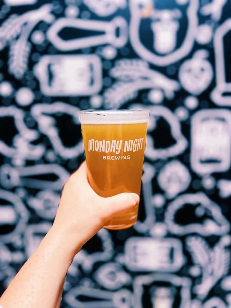 A hand holds a glass of beer with 'Monday Night Brewing' printed on it in Atlanta, Georgia.