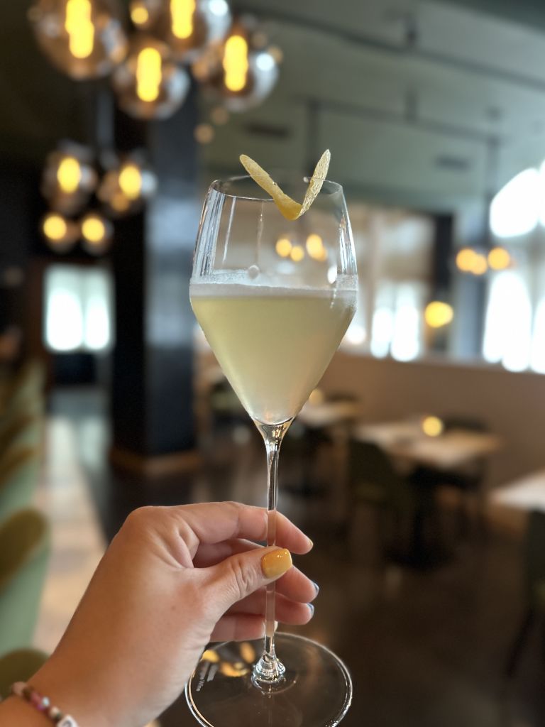 Must-Try Summer Cocktails in Atlanta 12 A hand holds a martini glass with a yellow drink and lemon peel garnish in Atlanta, Georgia.