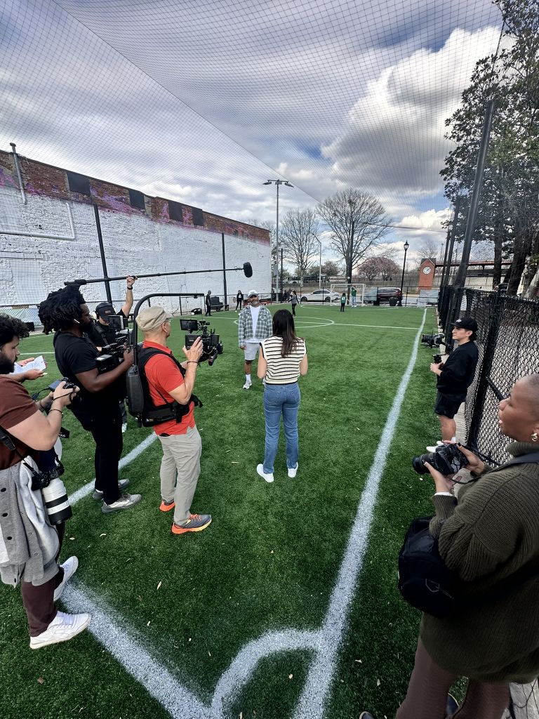 A film crew is setting up to shoot a scene on a soccer field with actors and equipment in Atlanta, Georgia.