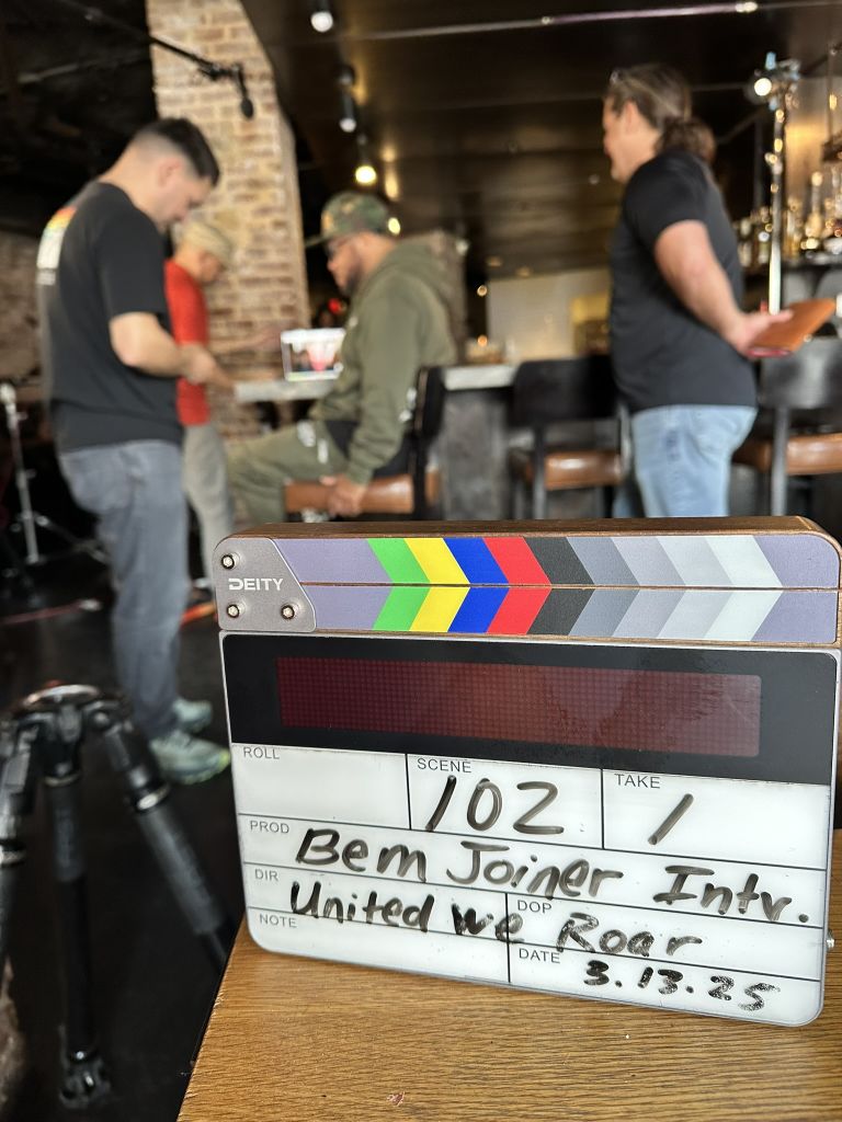 United We Roar 9 A clapperboard with the scene number 102 and the word 'Take' is placed on a wooden table in Atlanta, Georgia.