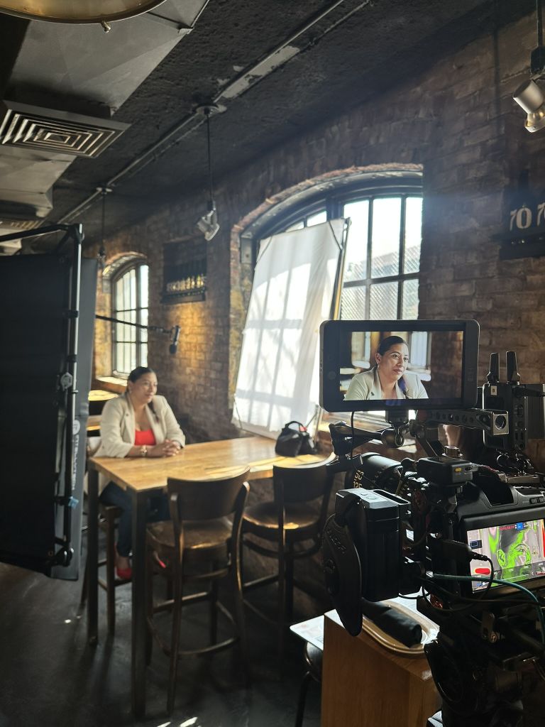 Woman in red shirt sits at wooden table in rustic studio with brick walls and large windows in Atlanta, Georgia.