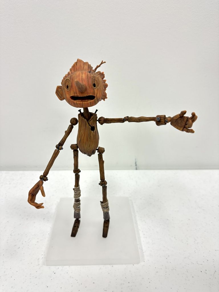 A wooden puppet with a carved pumpkin-like head, standing on a white base in Atlanta, Georgia.