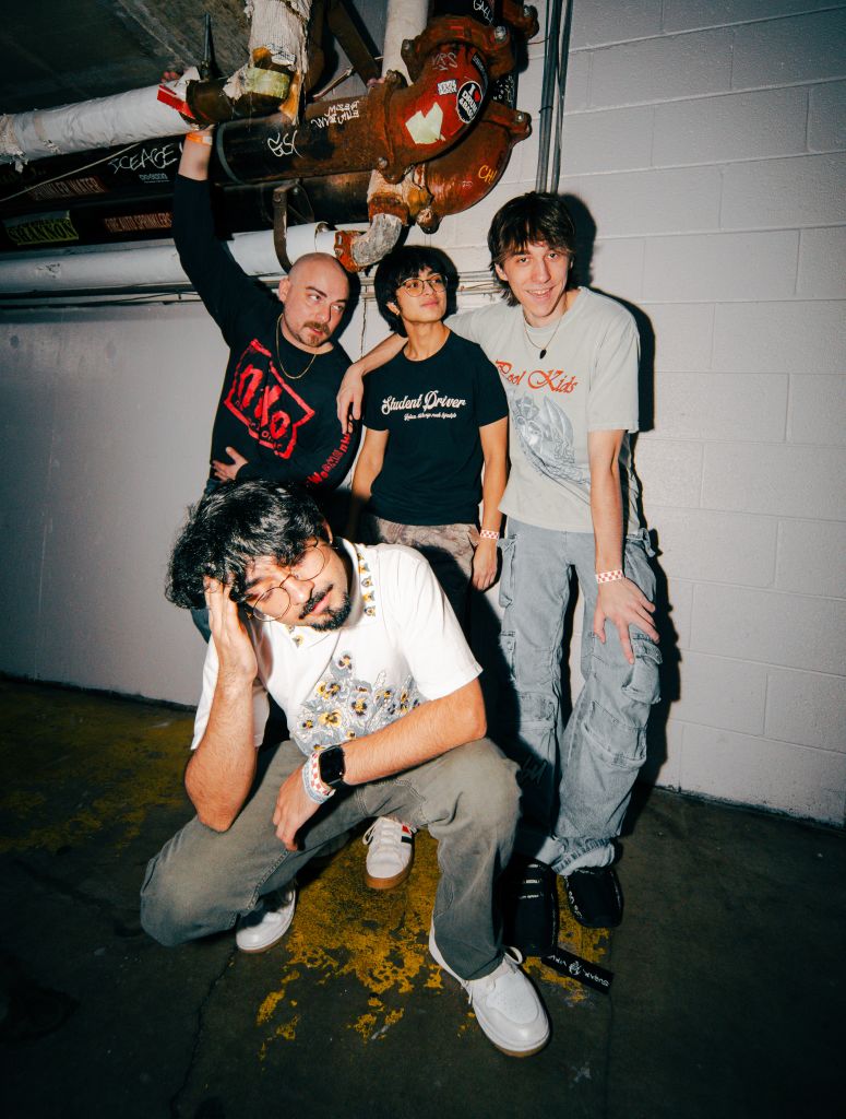 Ultimate Guide to Atlanta's Indie Music Scene 13 Four young men pose together in a dimly lit underground parking garage, surrounded by exposed pipes and graffiti-covered walls in Atlanta, Georgia.