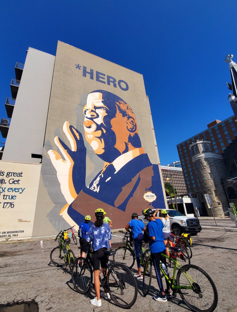 A group of people on bikes looking at a mural of John Lewis, with Bicycle Tours of Atlanta. 