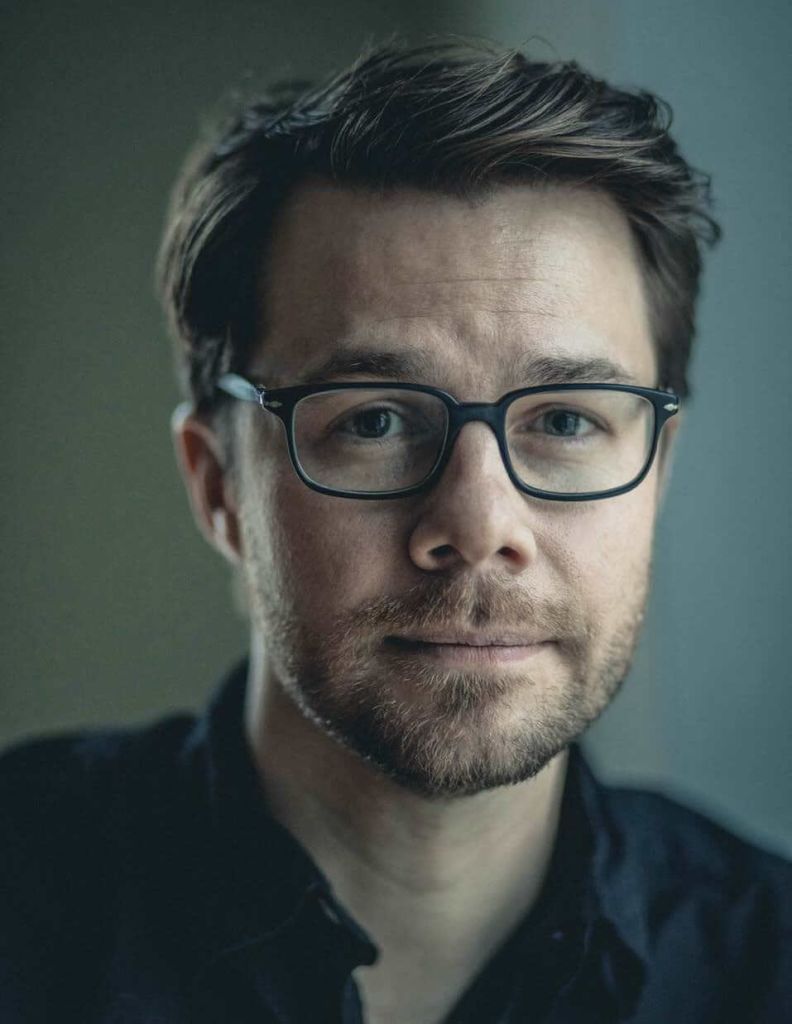A man with short dark hair, wearing black-rimmed glasses and a black shirt, looks directly at the camera with a neutral expression in Atlanta, Georgia.