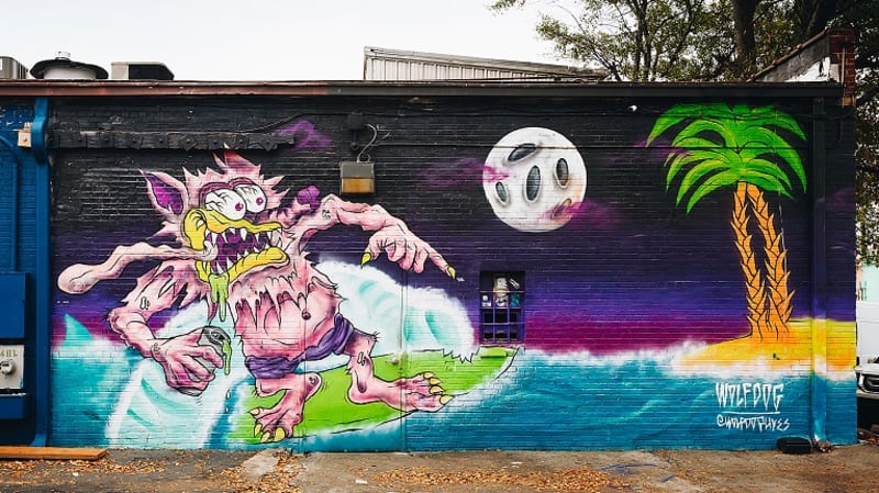 Cool, Funky Neighborhood: East Atlanta Village 5 A vibrant mural depicts a monstrous creature surfing on a wave beneath a full moon and palm trees in Atlanta, Georgia.