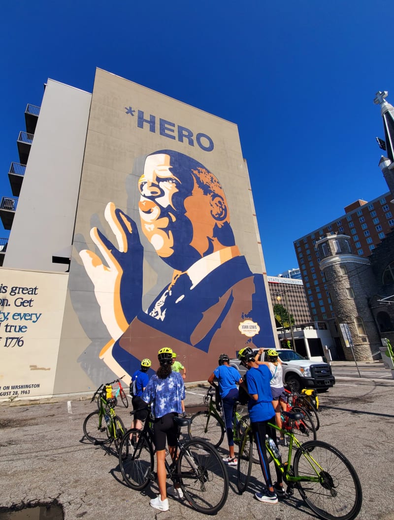 A group of people on bikes looking at a mural of John Lewis, with Bicycle Tours of Atlanta.