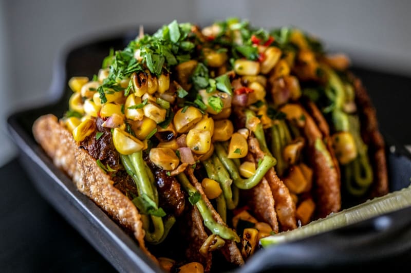 Black plate with 4 tacos in it, covered with corn and cilantro.