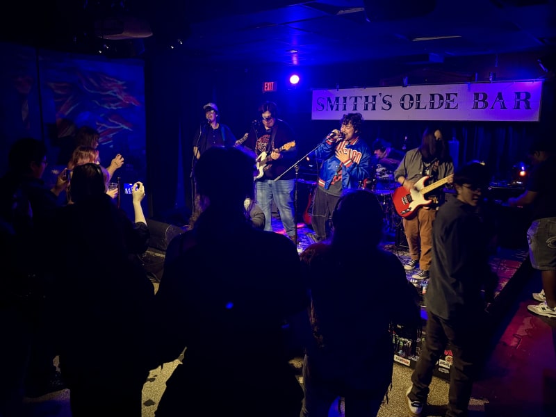 Ultimate Guide to Atlanta's Indie Music Scene 2 A lively band performs on a dimly lit stage at Smith's Olde Bar, with musicians playing guitars and a keyboard, while an enthusiastic crowd watches and records the show in Atlanta, Georgia.