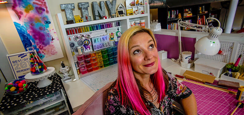 Karen Anderson 3 A woman with pink hair sits in a colorful craft room filled with art supplies and books in Atlanta, Georgia.