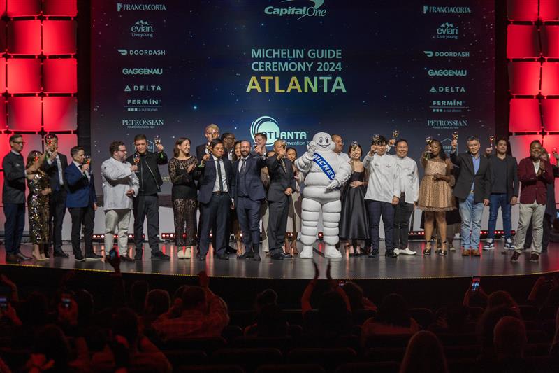 La Guía MICHELIN Regresa a Atlanta 13 A diverse group of people celebrate on stage with Michelin Man at an awards ceremony in Atlanta, Georgia.