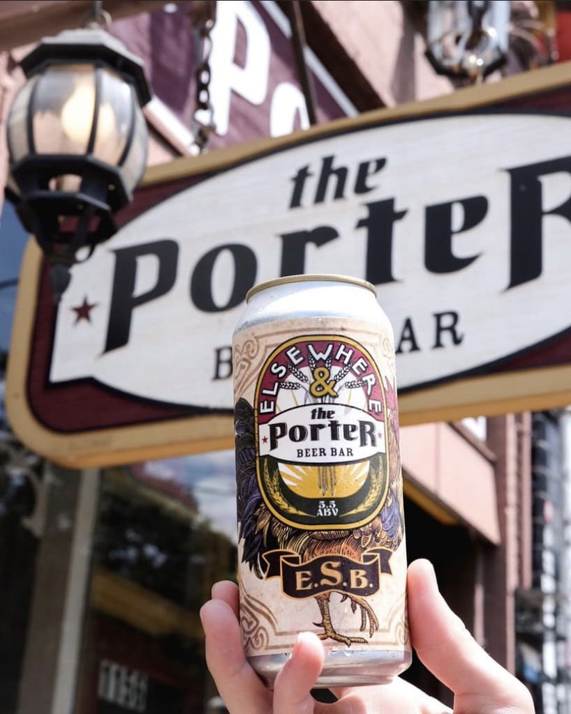 A hand holds a can of ElseWhere & The Porter beer in front of a bar sign in Atlanta, Georgia.