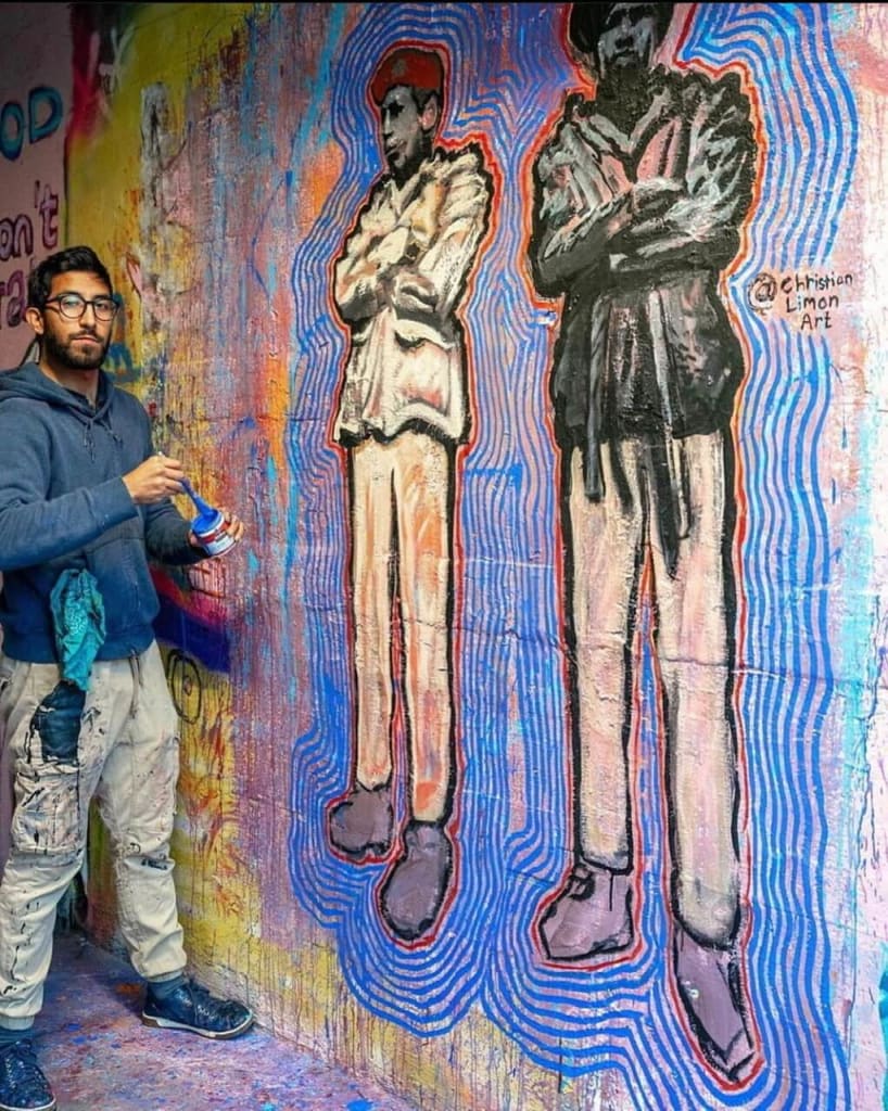A man paints a mural of two figures on a colorful, graffiti-covered wall in Atlanta, Georgia.