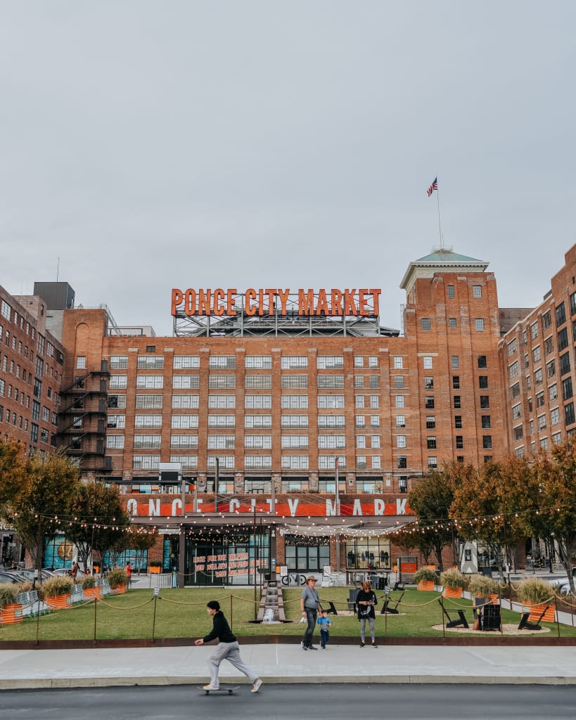 A skateboarder glides past the Ponce City Market, a bustling urban hub with vibrant signage and outdoor seating in Atlanta, Georgia.