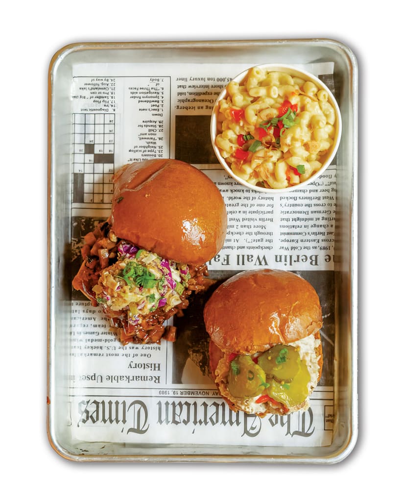 Two burgers with toppings and a side of macaroni salad on a tray lined with newspaper in Atlanta, Georgia.