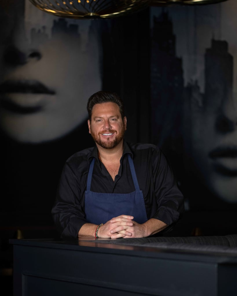 A smiling man in a black apron stands behind a dark counter in Atlanta, Georgia.