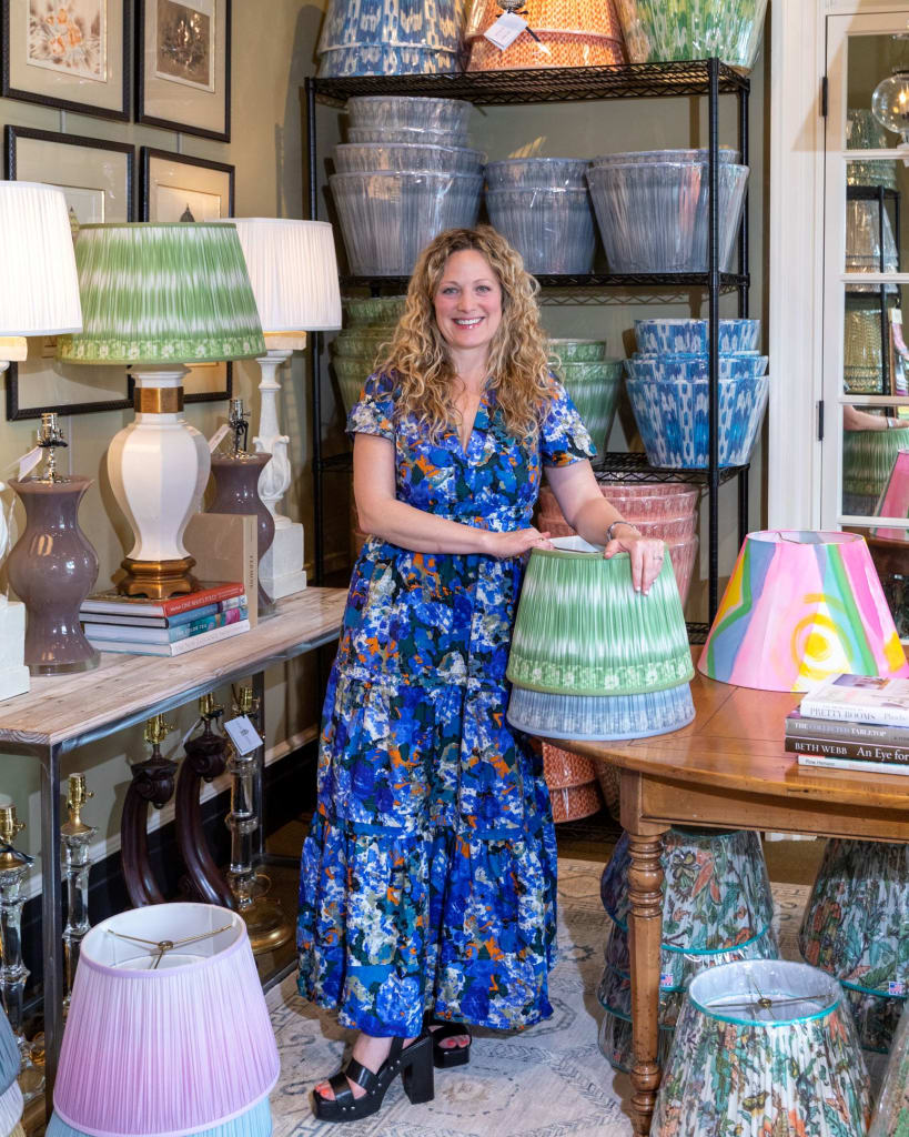 Woman in floral dress stands amidst colorful lampshades and home decor items in Atlanta, Georgia.