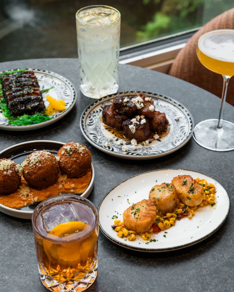 A table set with a variety of gourmet dishes and beverages, including fried appetizers, grilled meat, scallops, and cocktails in Atlanta, Georgia.