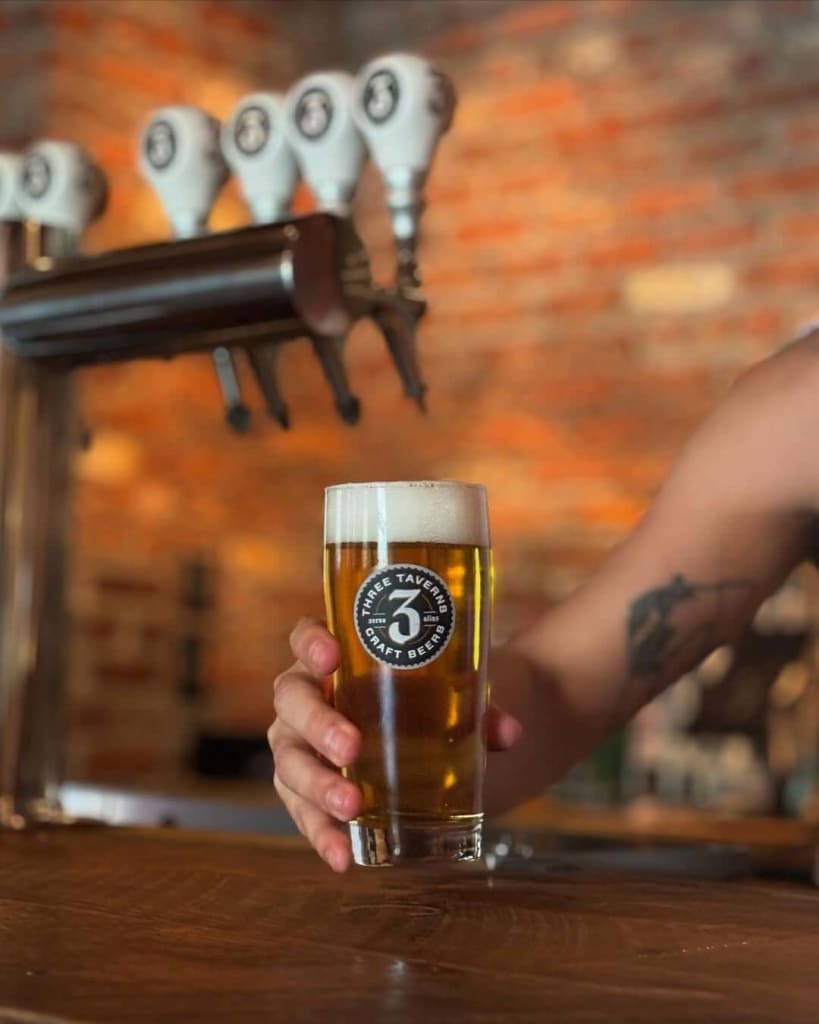 A hand holds a glass of beer with a logo, in front of a tap with multiple handles in Atlanta, Georgia.