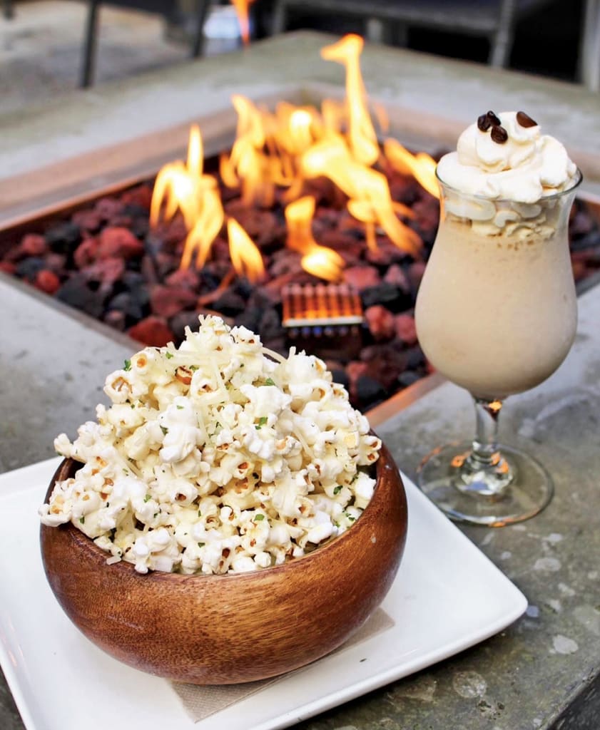 A bowl of garlic parmesan popcorn and a creamy coffee drink by a fire pit in Atlanta, Georgia.