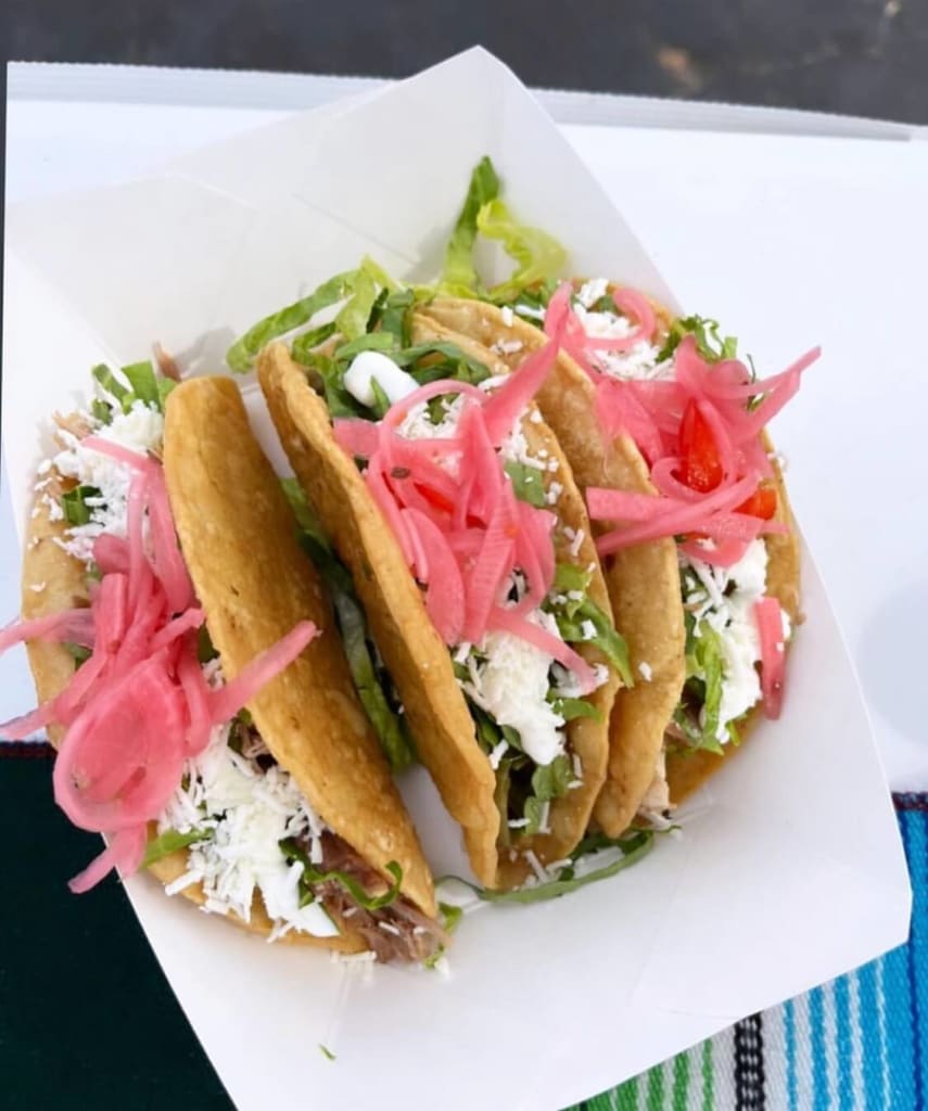 Three soft tacos with pink pickled onions, lettuce, and cheese in a white paper container in Atlanta, Georgia.